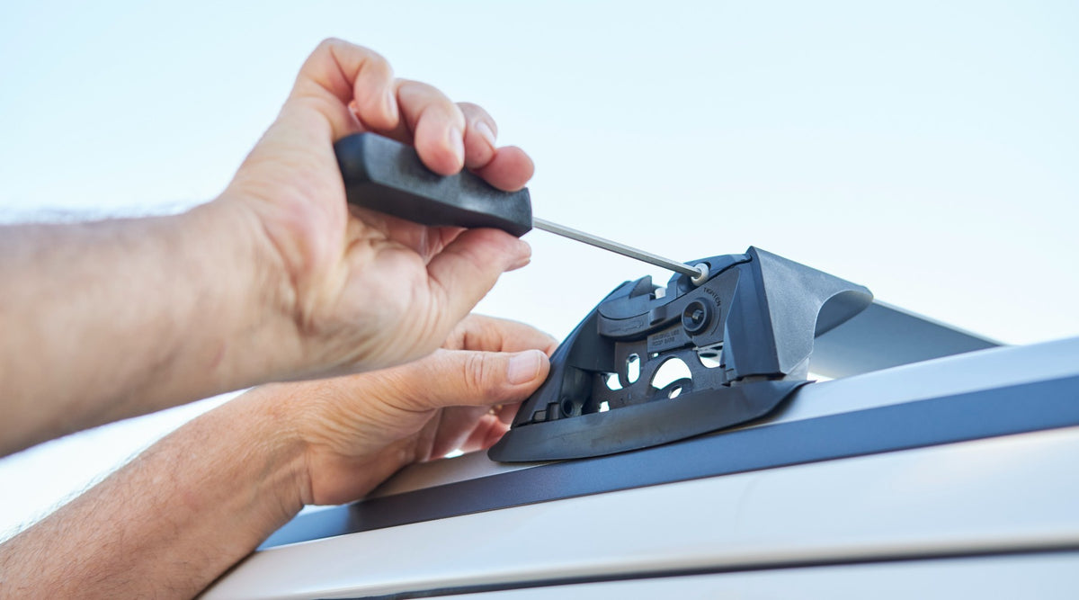 Hands using a hex key to tighten a roof rack foot onto a vehicle roof